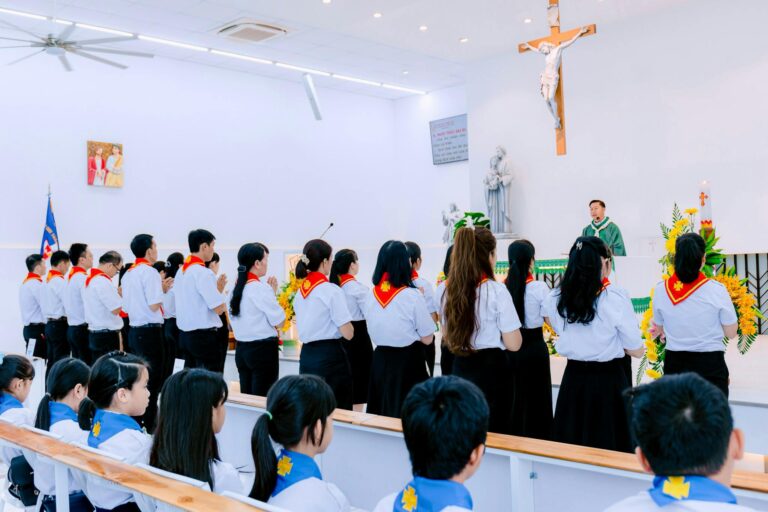 Congregation of youth gathered in a church service, wearing uniforms and listening to priest.